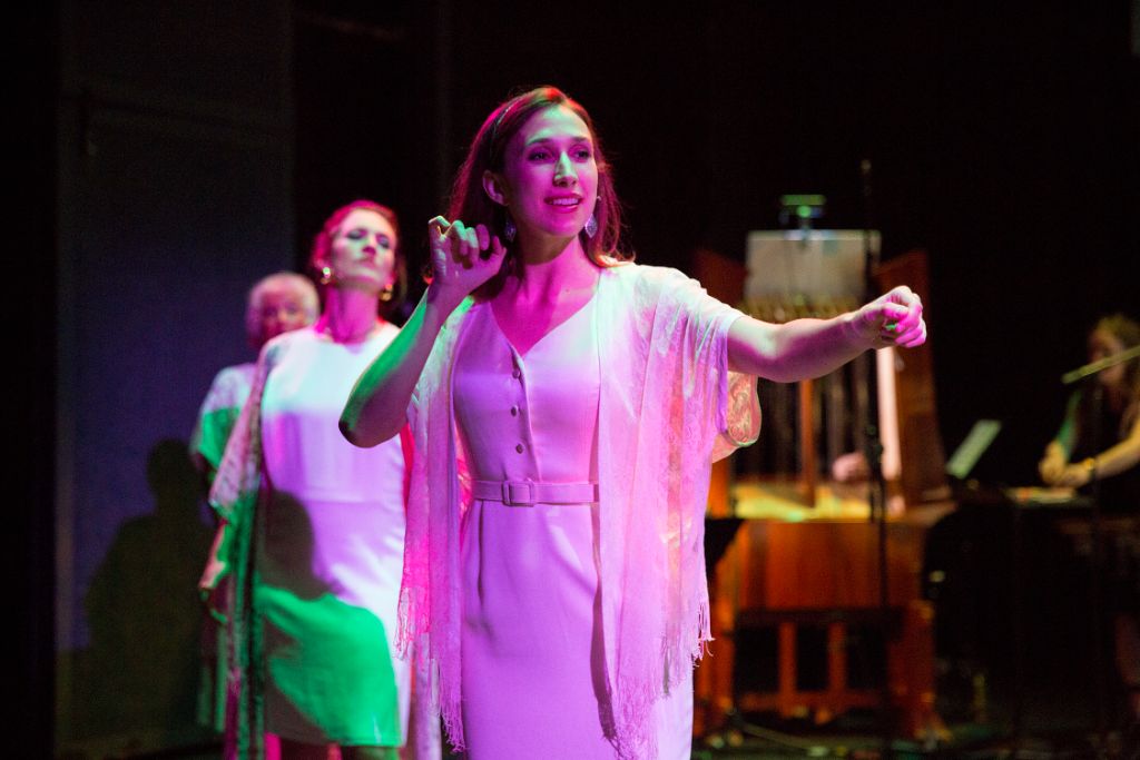 The LSD Trio in performance — three sopranos in white under dramatic pink and green stage lighting, with Harry Partch instruments visible in the background